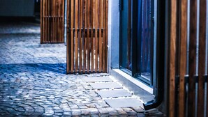 A cobblestone pathway leading to a building with a wooden fence and a glass door.