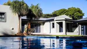 A modern house with a swimming pool, large windows, and a tree.