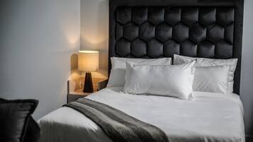 A neatly made bed with white linens, a dark headboard, and a bedside lamp.