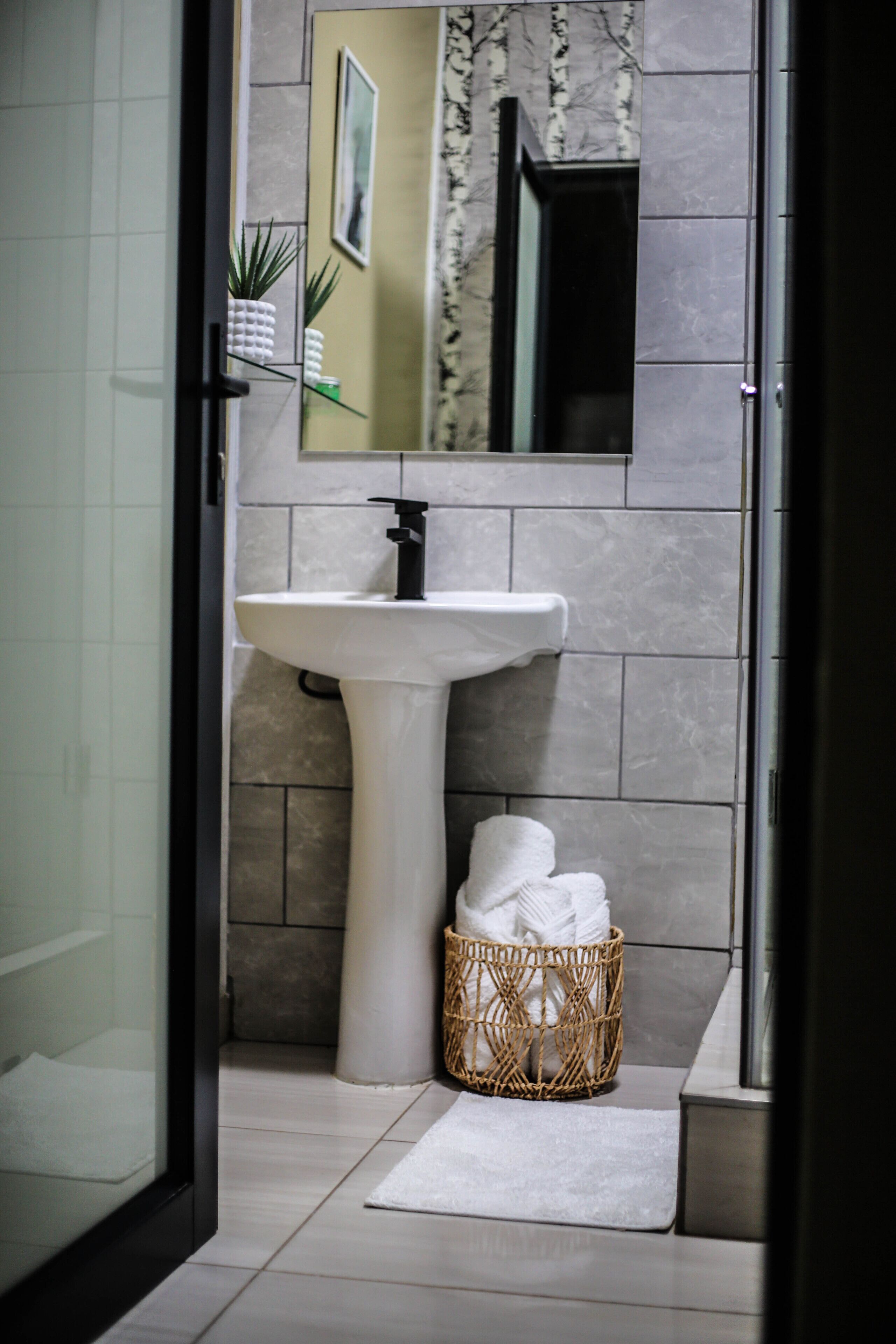 Une salle de bain avec un lavabo sur pied blanc, un miroir au-dessus, et un panier en osier contenant des serviettes, posé sur le sol.