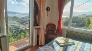 A bedroom with a bed, a chair, and a view of a landscape through a window. - Ai Canarbin  (Lerici)
