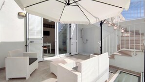 A spacious outdoor area with white wicker furniture, a large umbrella, and a glass door leading to a shower area. - Le Sorelle del Mare - Sole a 450m Dalla Spiaggia (Salve)