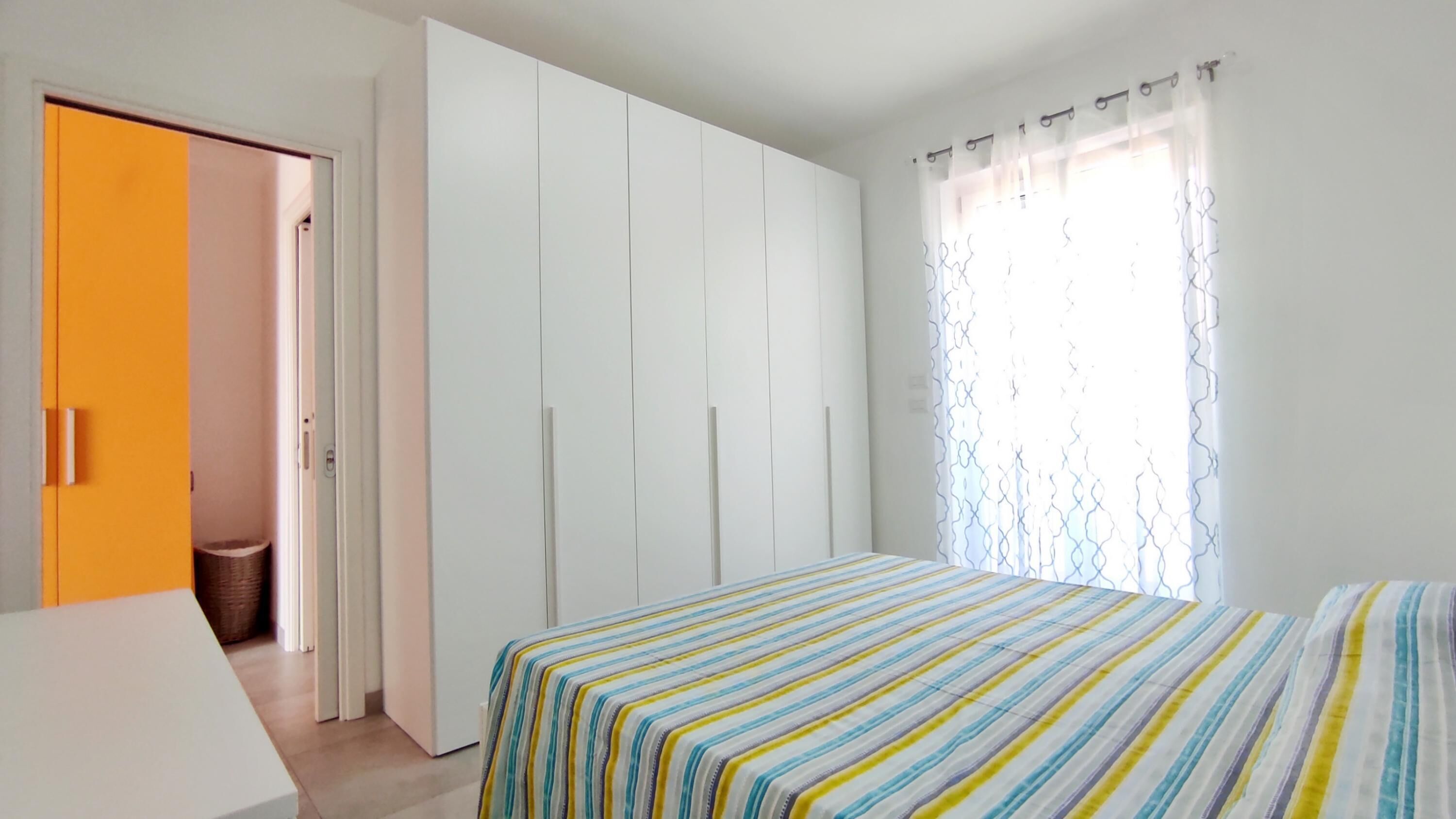 Un dormitorio con cama, armario y ventana con cortinas.