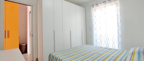 Un dormitorio con cama, armario y ventana con cortinas.