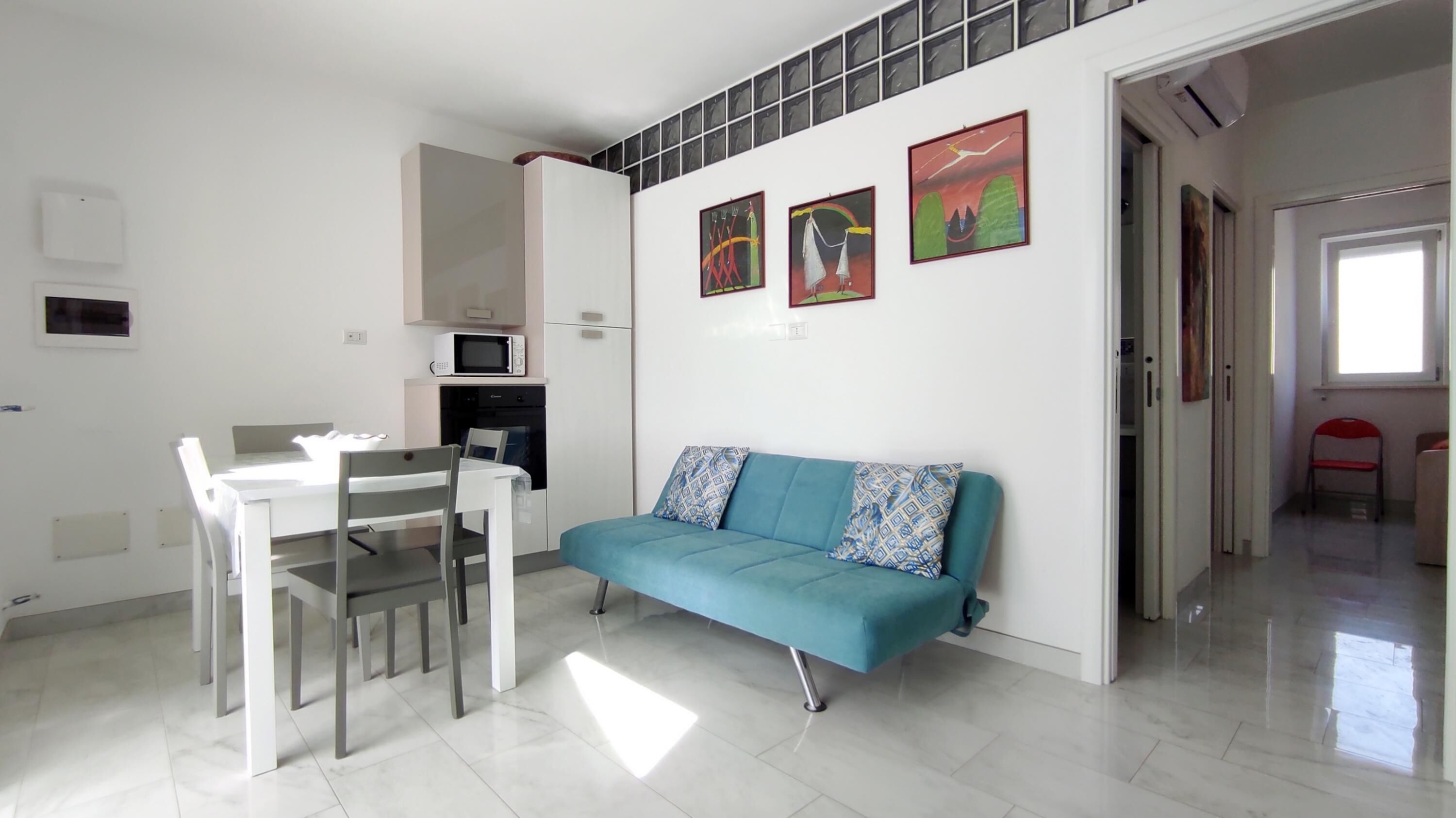 Uma sala de estar moderna com área de jantar, um sofá azul e um micro-ondas na parede.