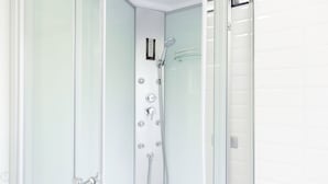 Un bany modern amb plat de dutxa envoltat de vidre, accessoris cromats i un panell de control.