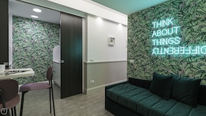 Habitació moderna amb un sofà verd, un escriptori amb una cadira i una paret amb paper pintat de temàtica tropical.