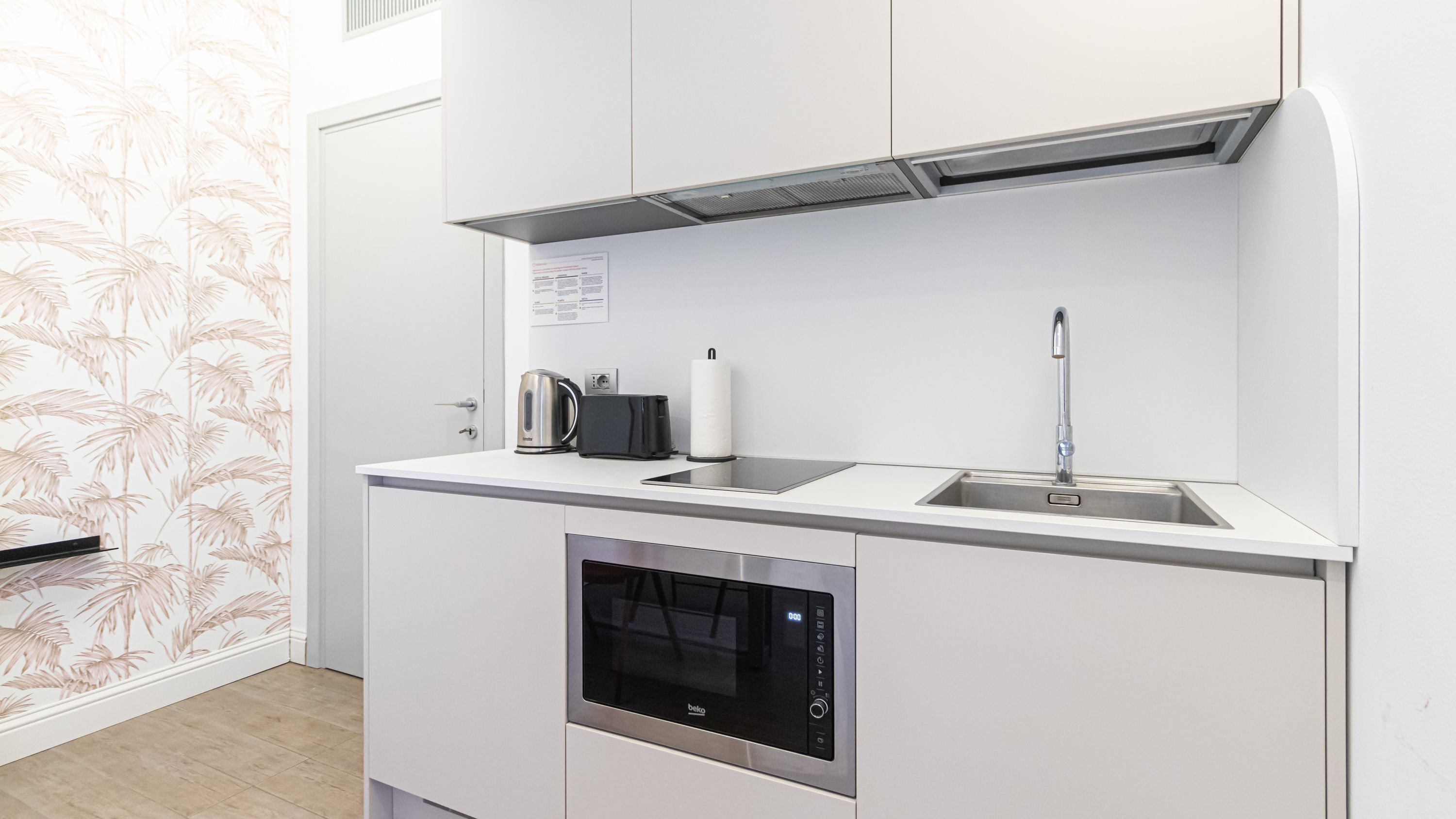 Una cocina moderna con horno empotrado, hervidor, tostadora y un lavabo.