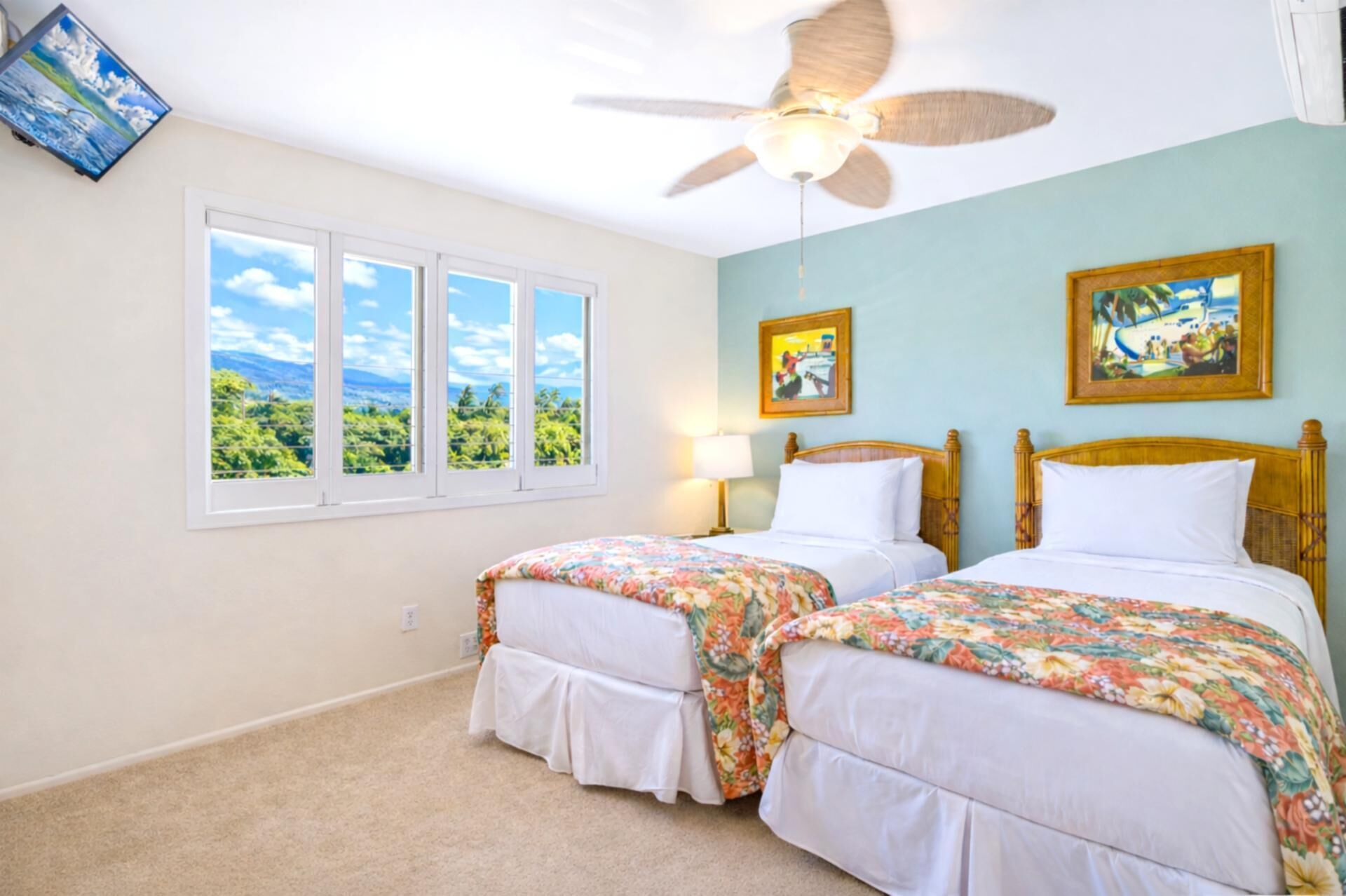 Habitación de hotel con dos camas, ventilador de techo, ventana grande con vistas y obras de arte en las paredes.