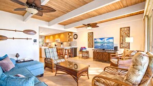 A spacious living area with a sofa, chairs, a coffee table, a TV, and a kitchen in the background. - Lokelani Resort by KBM (Napili-Honokowai)