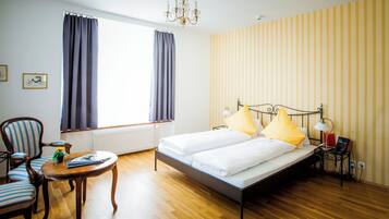 Una habitación de hotel con una cama, una silla, una mesa, una lámpara y un radiador.