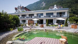 Hotel amb piscina, zona de seients a l'exterior i muntanyes al fons.