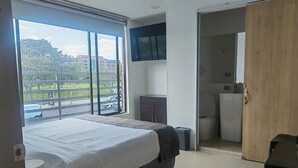 Habitación de hotel moderna con una cama grande, un televisor montado en la pared, un mueble pequeño y vistas al exterior a través de un ventanal.