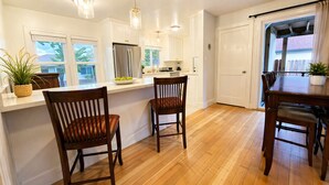 A kitchen with wooden flooring, white cabinets, a stainless steel refrigerator, and a dining area with two chairs. - Spacious 3BR Home - Near Downtown Martinez (Martinez)