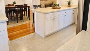 A modern kitchen with white cabinetry, a central island, pendant lighting, and a dining area with wooden chairs and a table. - Spacious 3BR Home - Near Downtown Martinez (Martinez)