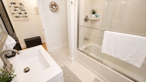 Baño con lavamanos blanco, cabina de ducha con mampara de vidrio y un perchero para toallas.