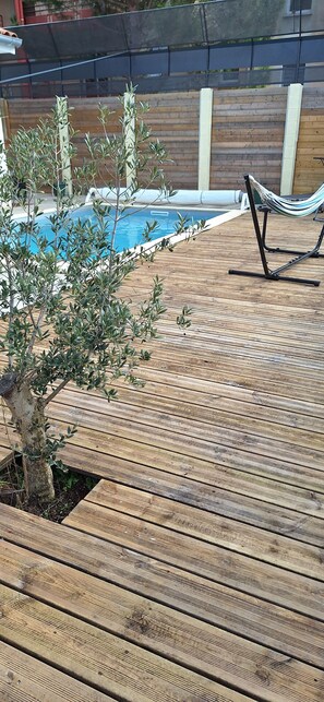 Eine Holzterrasse mit Pool, Hängematte und Olivenbäumen.
