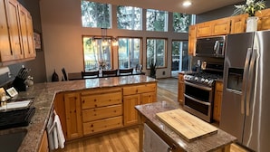 A modern kitchen with wooden cabinets, a granite countertop, stainless steel appliances, and large windows offering views of the outdoors. - Beautiful lakefront Casa del Lago on Lake Roesiger (Snohomish)