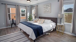 Une chambre à coucher avec un lit, un ventilateur de plafond, une fenêtre avec des rideaux, une chaise et une lampe.