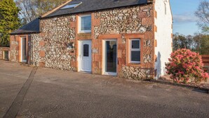 A stone cottage with a white door, two windows, and a small porch area. - 2 bedroom accommodation in Ruthwell, near Annan (Ruthwell, near Annan)