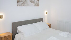 A neatly made bed with white linens, two bedside tables with lamps, and a beach-themed painting on the wall. - 2 bedroom accommodation in Ruthwell, near Annan (Ruthwell, near Annan)