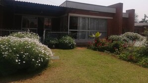 A modern house with a large window, a covered porch, and a well-maintained garden with various plants and flowers. - savanna guest house (Bulawayo)