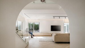 A modern living room with a large TV, a sofa, and a glass staircase leading to another level.
