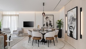 A modern living room with a round dining table, comfortable seating, a flat-screen TV, and artwork on the walls.