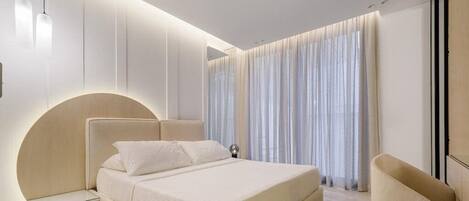 A modern bedroom with a large bed, a bedside table, a chair, and a large window with curtains.