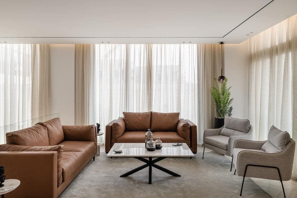 A modern living room with a brown leather sofa, a grey armchair, and a coffee table with decorative items.