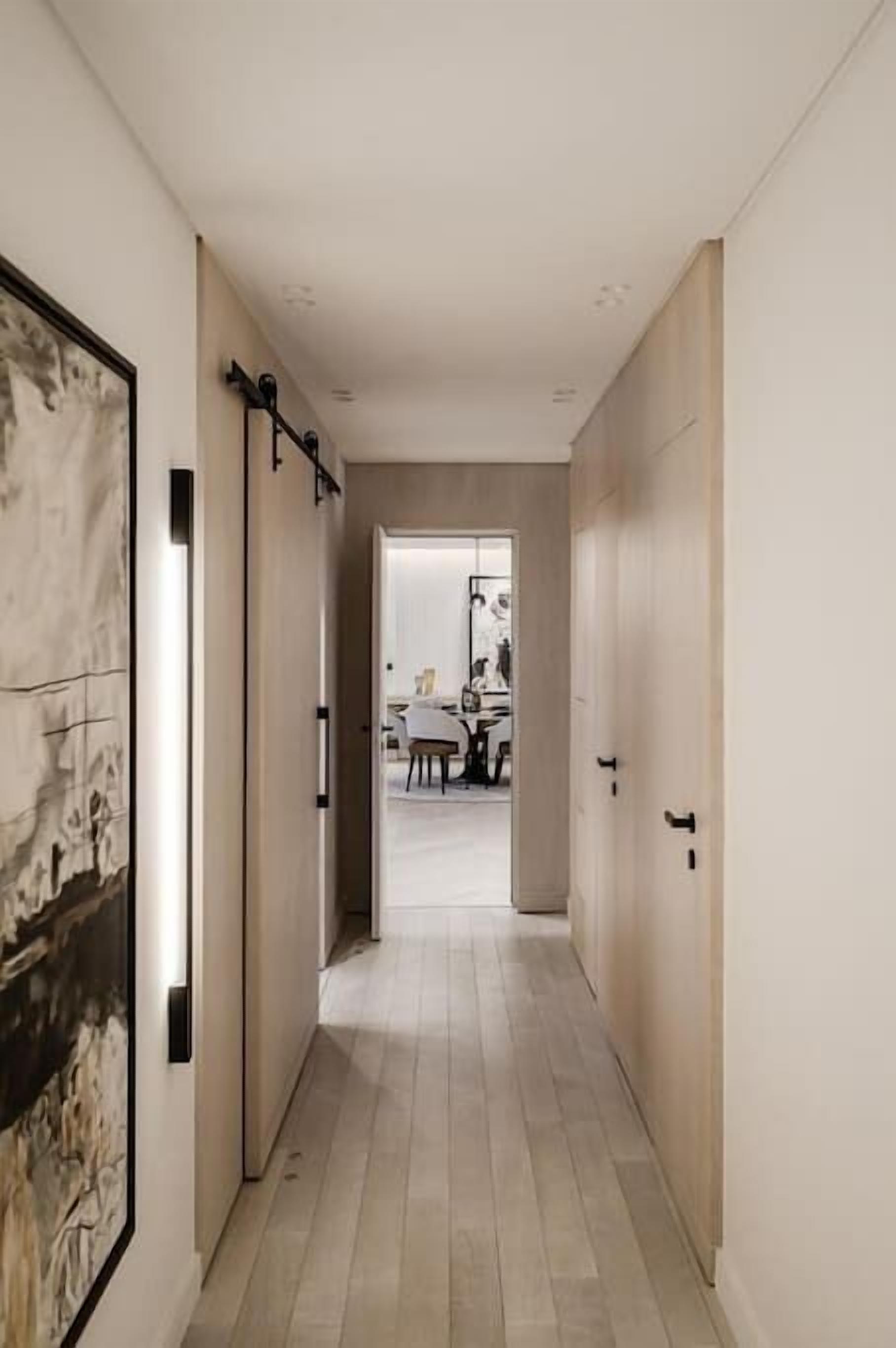 A hallway with a light wooden floor and a framed artwork on the left wall.