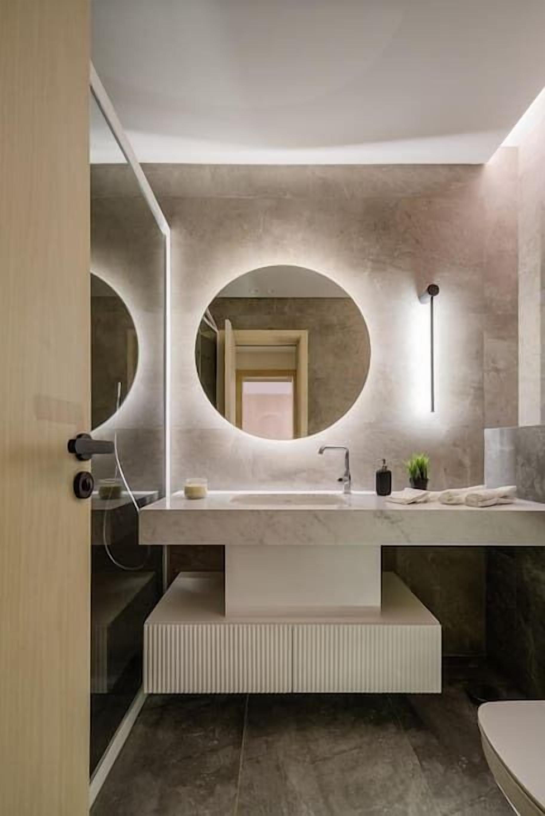 Un bagno moderno con un grande specchio ovale, un lavabo rettangolare e una panca integrata.
