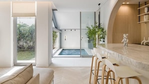 A modern interior with a glass-enclosed hot tub, a bar area with stools, and a view of the outdoors.