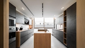 A modern kitchen with dark cabinetry, a central island, and built-in appliances.