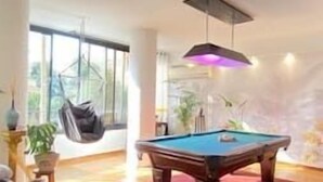 Una mesa de billar en una habitación con una mecedora, un tapete rojo y un ventanal grande.