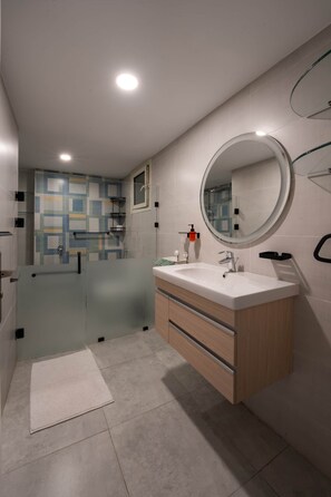 A modern bathroom with a glass shower enclosure, a round mirror, and a wooden vanity. - The Nile Vintage Haven (Al Gabalayah)