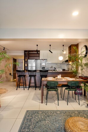 A modern kitchen with a central island, bar stools, and a dining table set for four. - The Nile Vintage Haven (Al Gabalayah)