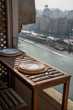 Una mesa con dos platos y cubiertos, con vistas a un río y edificios al fondo.