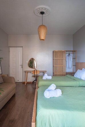 A bedroom with two beds, a wooden desk, a mirror, and a hanging robe rack. - The Nile Vintage Haven (Al Gabalayah)