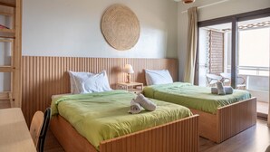 Ein Hotelzimmer mit zwei Betten, einem hölzernen Kopfteil, einer Wanddekoration aus Gewebe, einem kleinen Tisch mit Lampe sowie einem Balkon mit Stuhl.