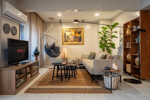 A living room with a sofa, TV, hanging chair, table, and bookshelf. - The Nile Vintage Haven (Al Gabalayah)
