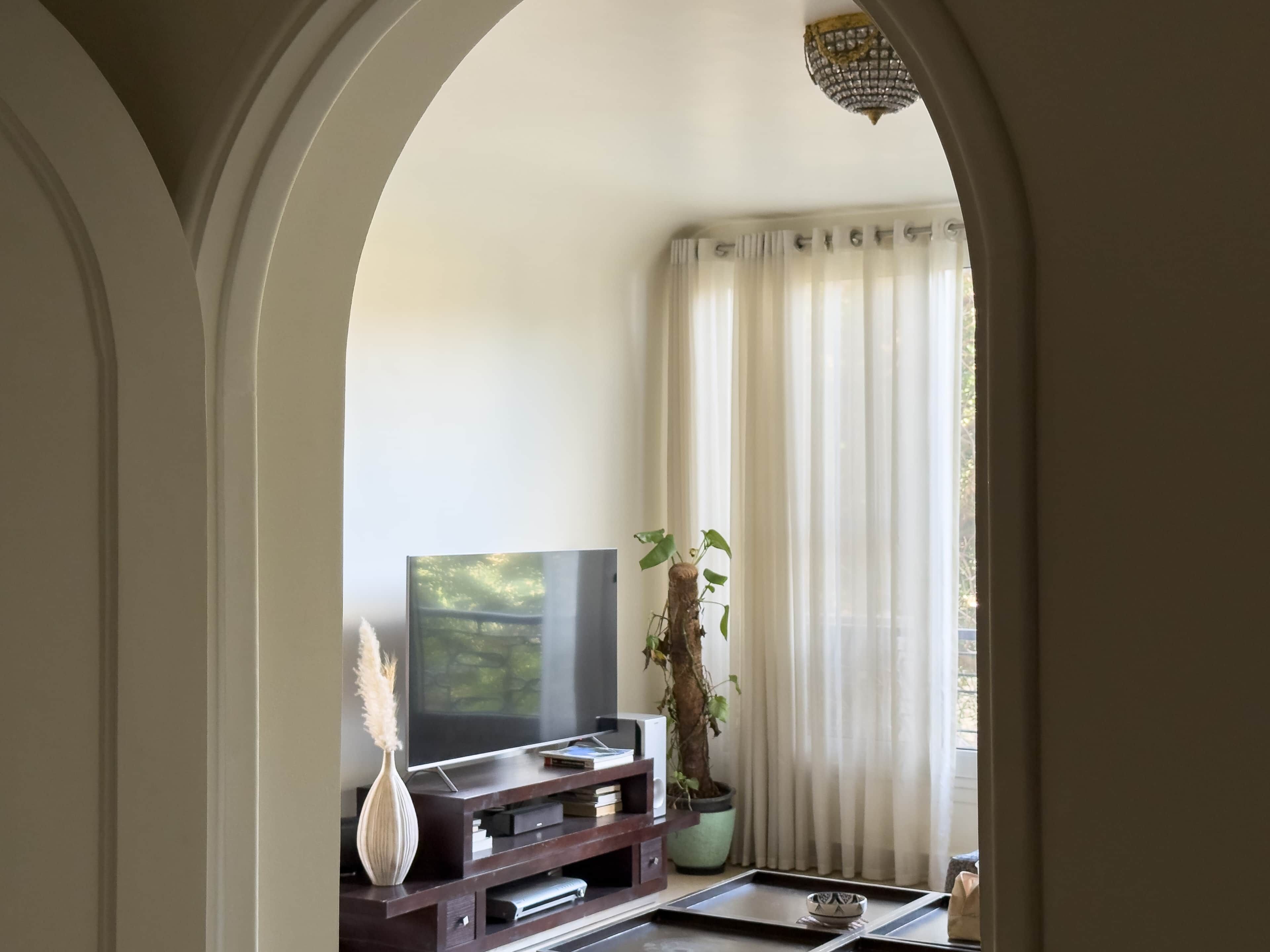 A living room with a TV, a plant, and a window with curtains.