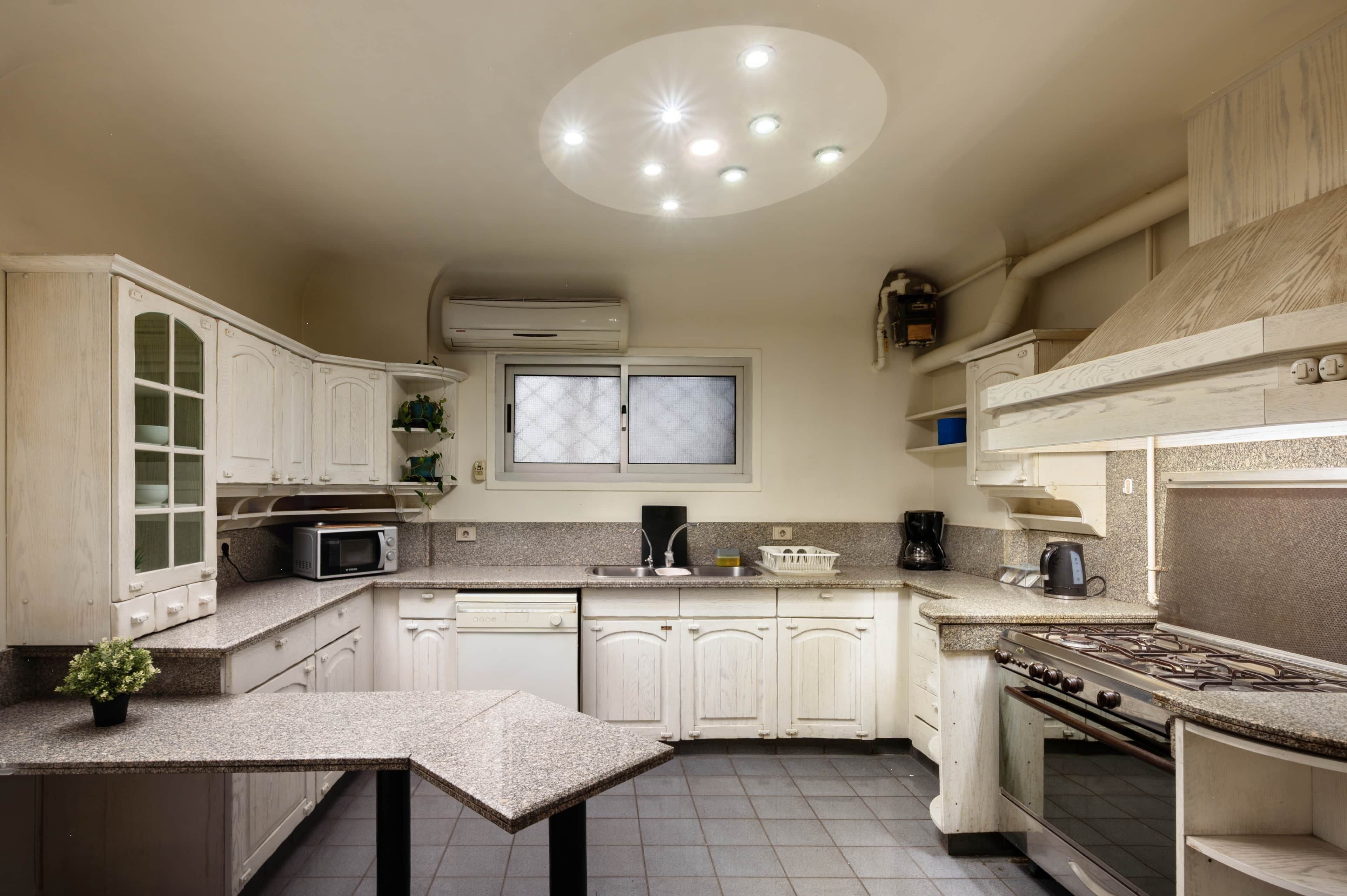 A kitchen with white cabinets, a microwave, a stove, and a window with blinds.