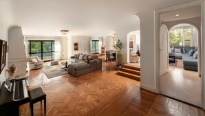 Ein großzügiger Wohnbereich mit Klavier, einem großen grauen Sofa und einem Essbereich im Hintergrund.