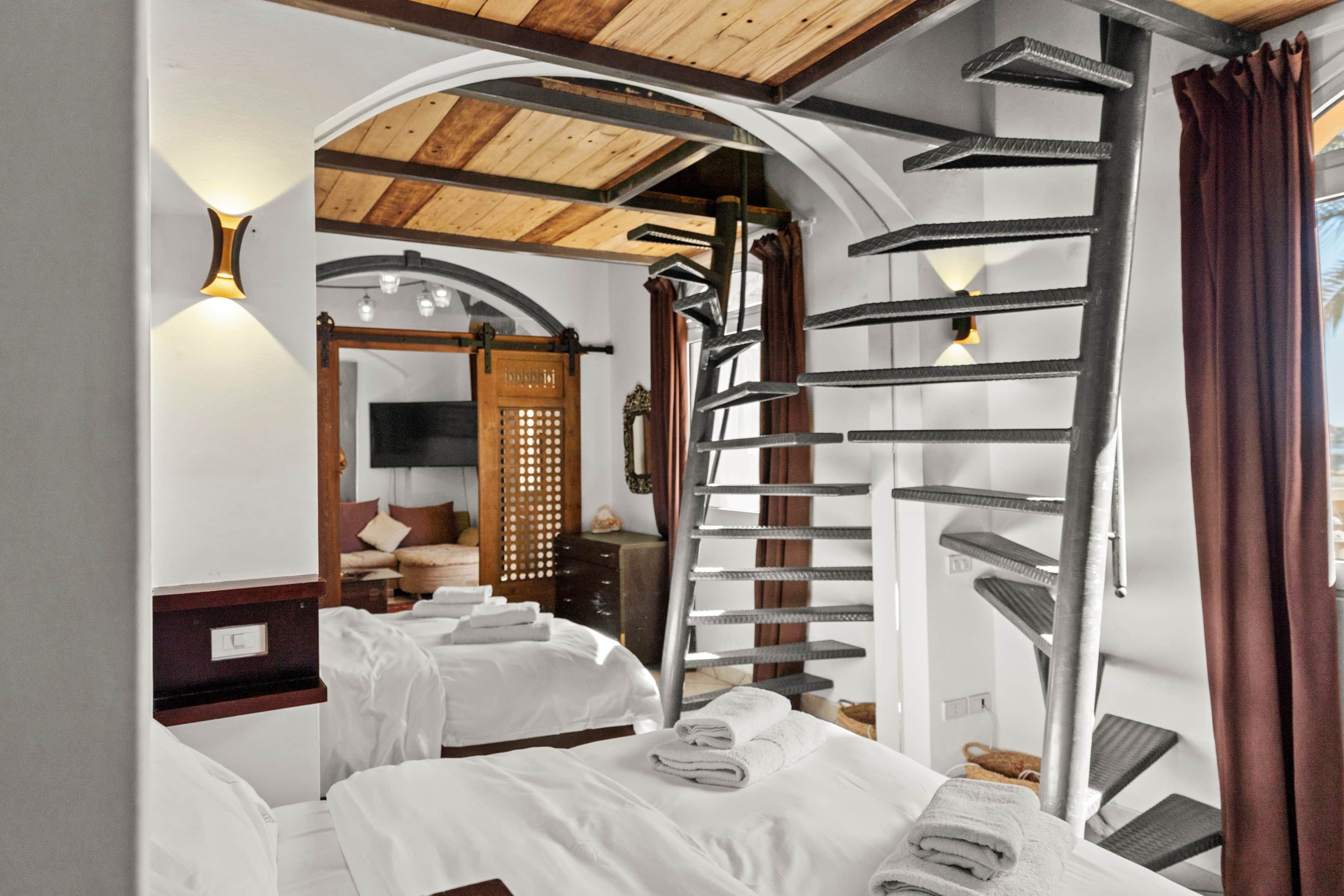 Habitación de hotel con dos camas, techo de madera, escalera de caracol y vistas al exterior.