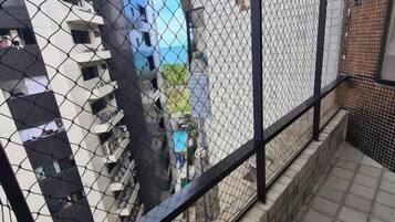 Una cerca de malla con baranda metálica negra, suelo de baldosas y vista a un edificio con varios balcones.
