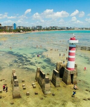 A coastal area with a lighthouse, clear waters, and a sandy beach.