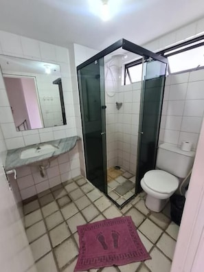 A bathroom with a glass-enclosed shower, a toilet, and a sink with a mirror above it.