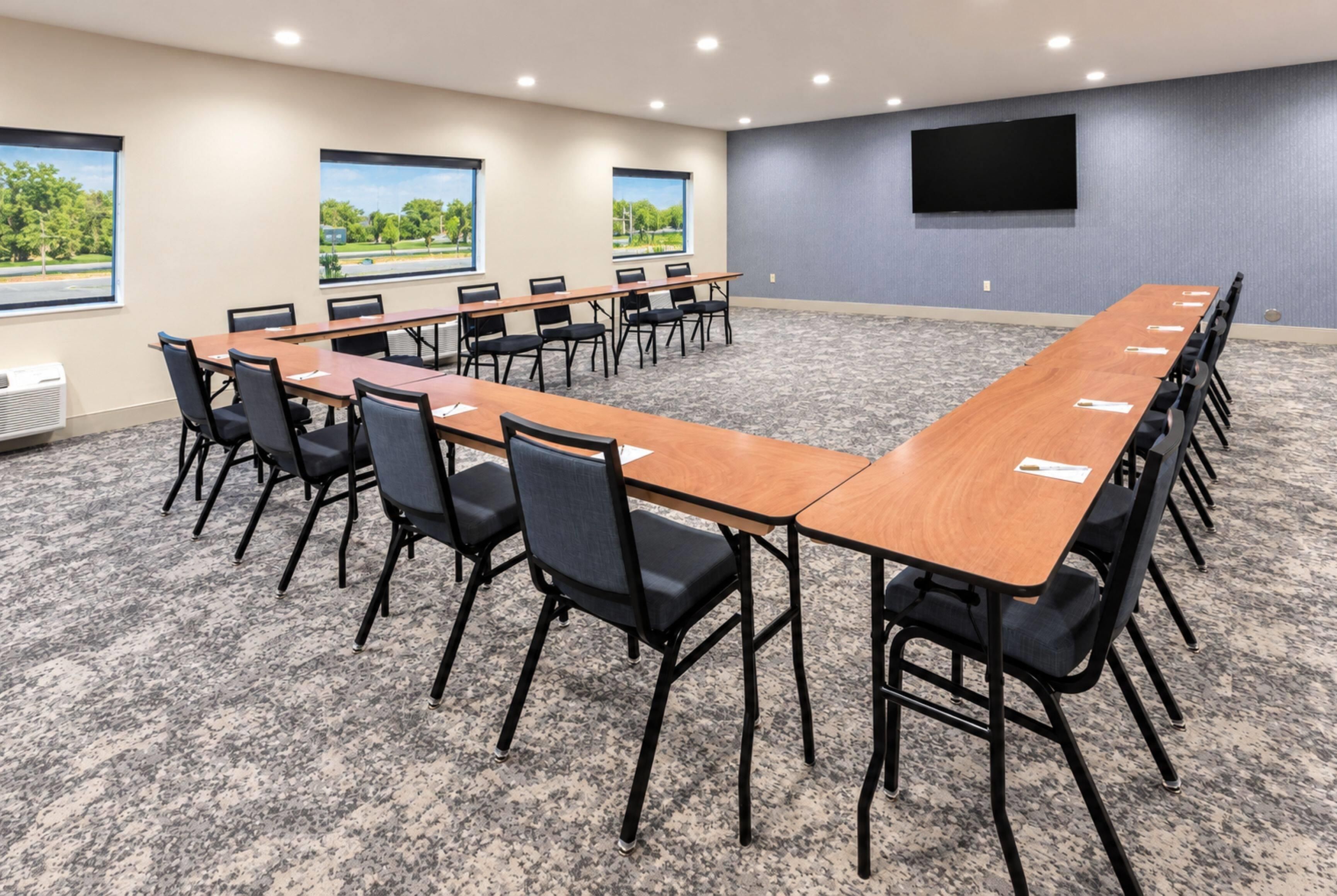 Un salón de conferencias con una mesa larga, sillas, un televisor de pantalla plana y ventanas con vista a zonas verdes.