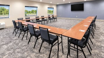 Un salón de conferencias con una mesa larga, sillas, un televisor de pantalla plana y ventanas con vista a zonas verdes.